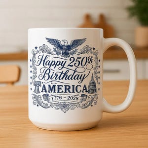 May include: White ceramic mug with a large handle. The mug features a blue design with the text "Happy 250th Birthday AMERICA" and the years 1776-2026. The design includes an eagle, stars, and the Capitol building.