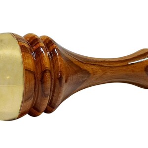 May include: A wooden massage tool with a brass head. The handle is a rich brown color with a smooth, polished finish. The brass head is a light gold color. The tool is designed for massage and relaxation.