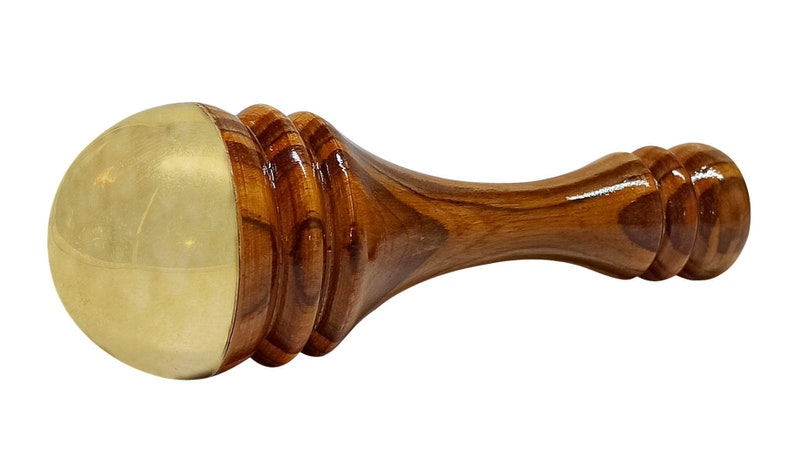 May include: A wooden massage tool with a brass head. The handle is a rich brown color with a smooth, polished finish. The brass head is a light gold color. The tool is designed for massage and relaxation.