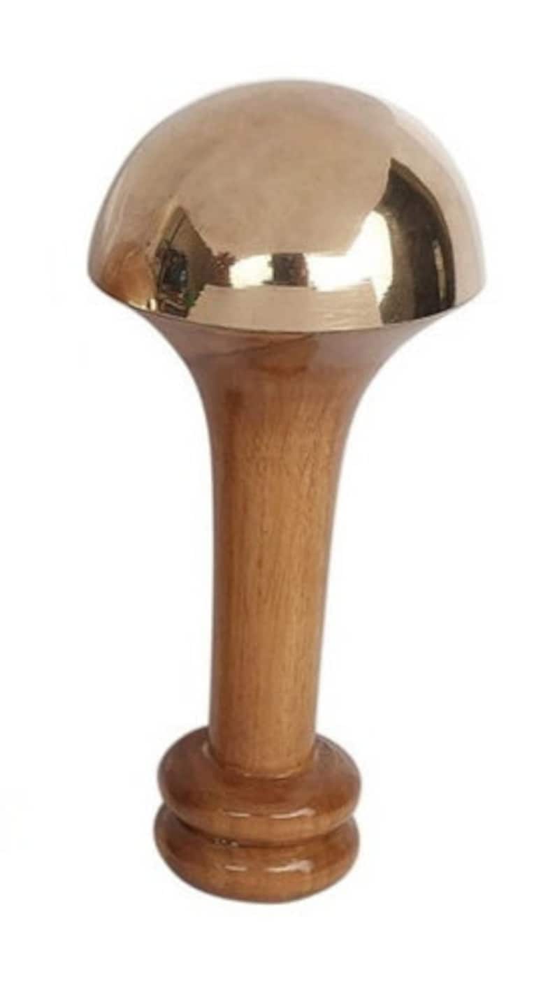 May include: A decorative bottle stopper with a polished brass dome and a wooden stem. The stem is a light brown color and has a flared shape. The base of the stopper has a rounded design.