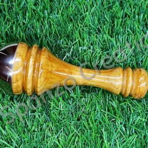 May include: A wooden massage tool with a polished, metallic ball at one end. The handle is a light brown color with a smooth, rounded design. The tool is designed for massage and relaxation.