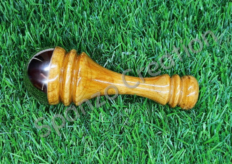May include: A wooden massage tool with a polished, metallic ball at one end. The handle is a light brown color with a smooth, rounded design. The tool is designed for massage and relaxation.