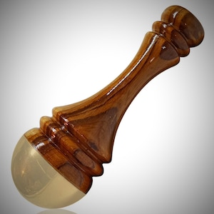 May include: A handcrafted wooden bottle stopper with a polished finish. The stopper features a light brown, curved wooden handle and a rounded, gold-colored base. The wood grain is visible, adding to its natural aesthetic.