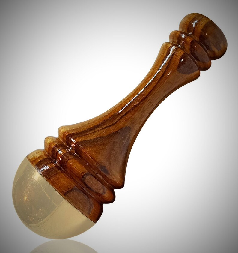 May include: A handcrafted wooden bottle stopper with a polished finish. The stopper features a light brown, curved wooden handle and a rounded, gold-colored base. The wood grain is visible, adding to its natural aesthetic.