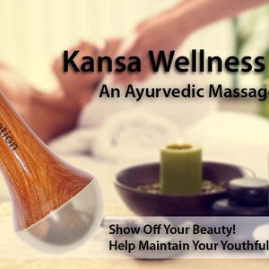 May include: A wooden Kansa Wellness Wand with a rounded top and a silver-colored base. The wand is labeled "Spanzo Creation" and is designed as an Ayurvedic massage tool. The image also includes a lit candle and a bowl.