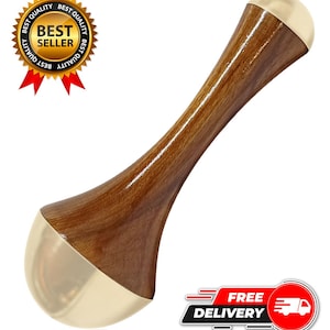 Puede incluir: Una herramienta de masaje de madera con un acabado pulido marrón y extremos de metal dorado. La herramienta tiene un diseño curvo y ergonómico. La imagen también incluye una insignia de "Más vendido" y un gráfico de "Entrega gratuita".