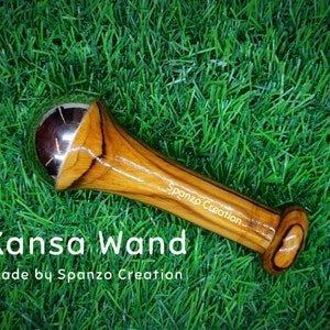 May include: A Kansa wand with a polished metal sphere and a wooden handle. The handle is made of light brown wood with dark brown grain patterns. The text "Kansa Wand" and "Made by Spanzo Creation" are visible.