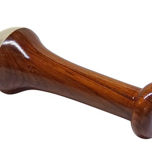 May include: A wooden pestle with a polished finish. The pestle has a cylindrical handle and a rounded head with a brass-colored cap. The opposite end is also rounded. The wood grain is visible.