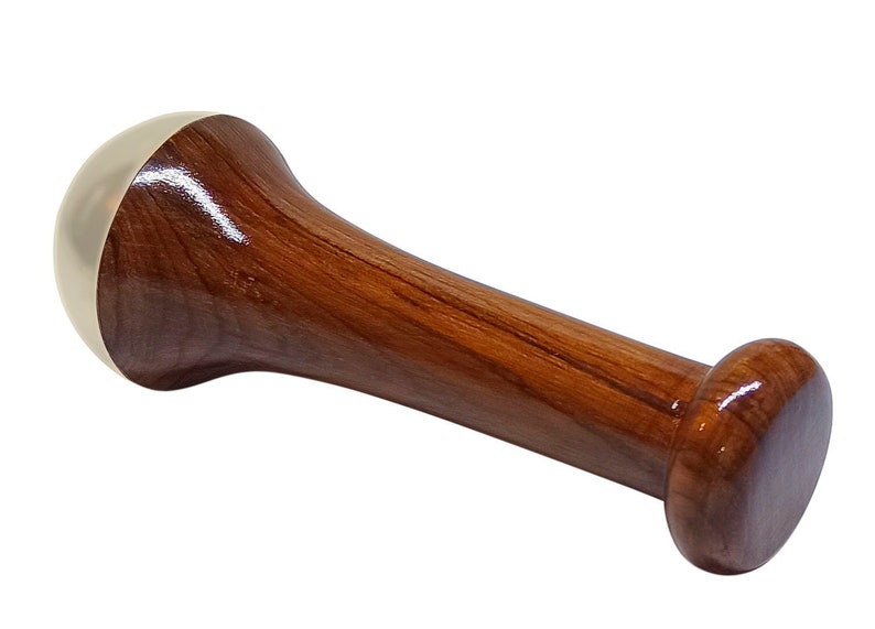 May include: A wooden pestle with a polished finish. The pestle has a cylindrical handle and a rounded head with a brass-colored cap. The opposite end is also rounded. The wood grain is visible.