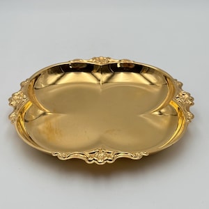 May include: A gold-colored, four-sectioned serving tray with ornate floral detailing around the rim. The tray has a glossy finish and a symmetrical, clover-like shape, suitable for serving appetizers or small items.