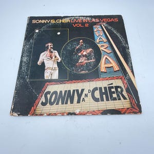 May include: Vintage vinyl record album cover for "Sonny & Cher Live in Las Vegas Vol. 2." The cover features images of Sonny and Cher, with the Sahara hotel sign in the background. The album title and artist names are prominently displayed.