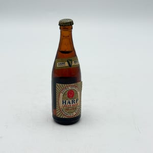 May include: A small, brown glass bottle of Harp Lager Beer with a gold cap. The label features the Harp logo and the words "Extra Quality" and "Imported Beer."