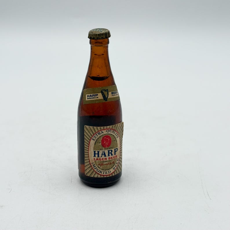 May include: A small, brown glass bottle of Harp Lager Beer with a gold cap. The label features the Harp logo and the words "Extra Quality" and "Imported Beer."