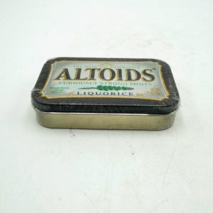 May include: A rectangular tin of Altoids liquorice mints. The tin is black with a gold border and a label that reads "Altoids, Curiously Strong Mints, Liquorice". The net weight is 1.76 oz (50g).