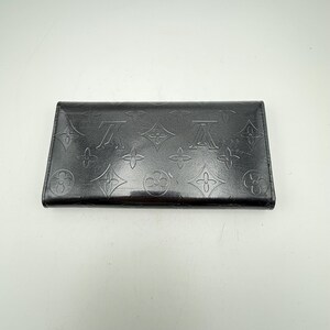 Puede incluir: Cartera de cuero negro con estampado de monograma en relieve. La cartera rectangular presenta un patr&oacute;n repetido del logotipo de la marca. El cuero tiene un acabado brillante y la cartera parece estar cerrada.