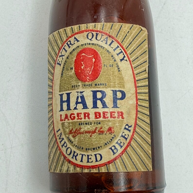 May include: A brown glass bottle with a label featuring the text "H&Auml;RP LAGER BEER." The label has a red emblem and is surrounded by text that reads "IMPORTED BEER" and "EXTRA QUALITY."