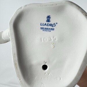 May include: A close-up of the bottom of a white porcelain figurine. The base features the blue "LLADR&Oacute;" logo, "HAND MADE IN SPAIN", and the number "1035".