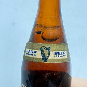 May include: A brown glass beer bottle with a label that reads "Harp Brewed in Ireland Beer." The label features a harp symbol. The bottle has a dark amber color.