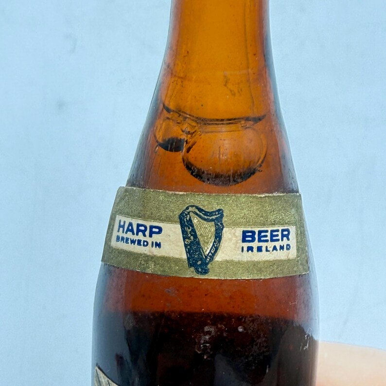 May include: A brown glass beer bottle with a label that reads "Harp Brewed in Ireland Beer." The label features a harp symbol. The bottle has a dark amber color.