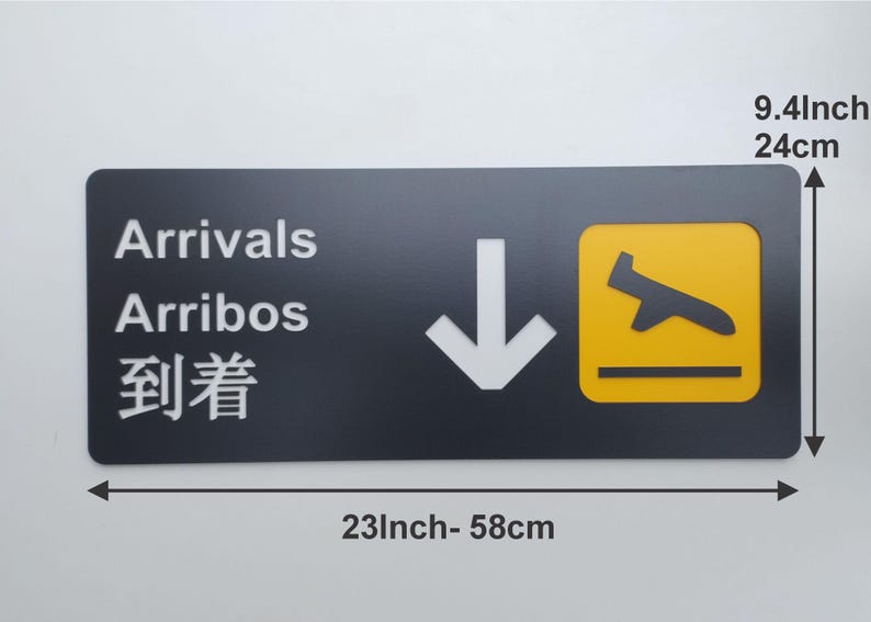 May include: Black and yellow airport sign with white text that reads "Arrivals", "Arribos", and "到着".  The sign also has a white downward arrow and a yellow airplane icon. The sign is 23 inches wide and 9.4 inches tall.