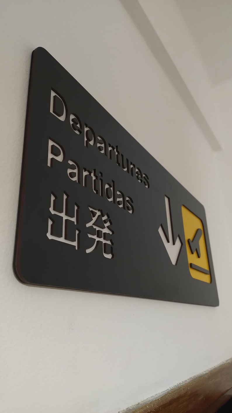 May include: Black sign with white text that reads "Departures, Partidas, 出発" with a yellow arrow pointing down and a small airplane icon.