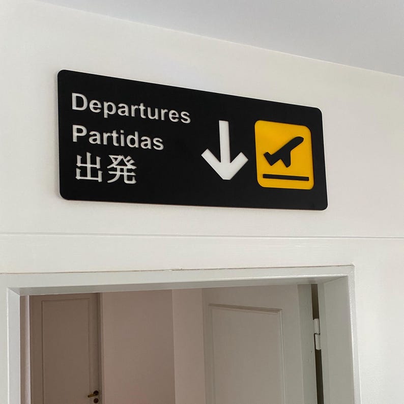 May include: Black and yellow sign with white text that reads "Departures, Partidas, 出発" with a white arrow pointing down and a yellow airplane icon.