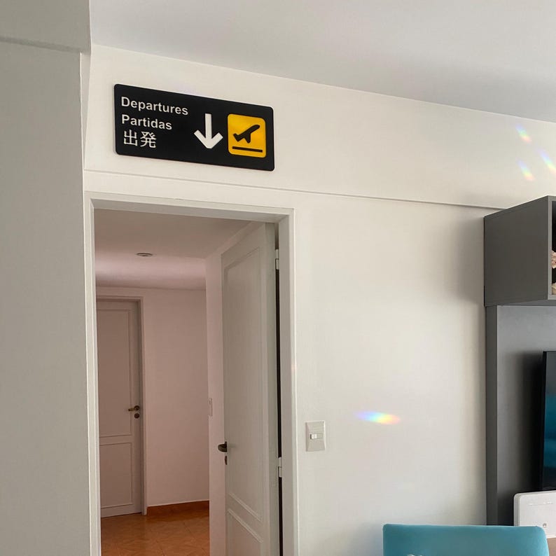 May include: A black and yellow sign with an airplane icon and an arrow pointing down. The sign reads "Departures, Partidas, 出発".