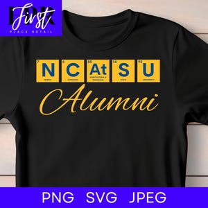 Puede incluir: Una camiseta negra con un diseño gráfico de cinco cuadrados amarillos que contienen letras y números azules, imitando elementos de la tabla periódica. El texto dice N, C, At, S, U, con la palabra Alumni escrita en cursiva amarilla debajo.