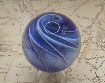 May include: A blue and white swirl glass marble on a clear glass stand. The marble has a white swirl pattern on a blue background.