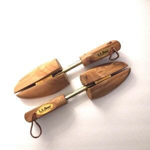 May include: Two wooden shoe trees with metal rods and leather loops. The shoe trees are made of light-colored wood and feature the "L.L.Bean Freeport, Maine" logo. The shoe trees are designed to maintain the shape of shoes.