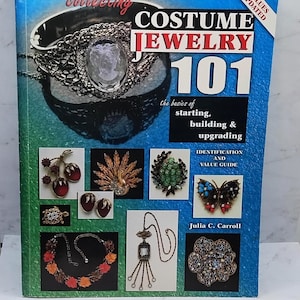 May include: A book titled "Costume Jewelry 101" with a blue and green cover. The cover features a silver-toned cameo pendant and various costume jewelry pieces. The book's subtitle is "the basics of starting, building & upgrading."