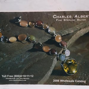 May include: A catalog cover featuring a necklace with oval-shaped gemstones in various colors, including brown, beige, and green, set in silver. The necklace has a large, yellow-green pendant. The text "CHARLES ALBERT FINE STERLING SILVER" is displayed at the top.