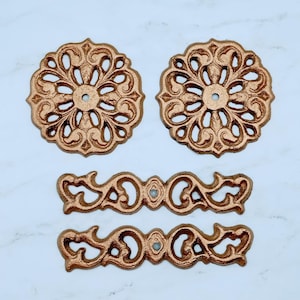 May include: Two ornate, gold-colored metal decorative pieces with a circular design and two smaller, gold-colored metal decorative pieces with a curved design.