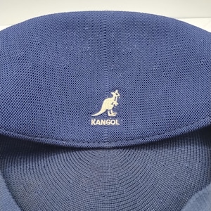 Op de afbeelding: Een donkerblauwe Kangol-pet van getextureerde gebreide stof met een opvallend geborduurd logo aan de voorzijde. Het logo toont een wit kangoeroesilhouet boven het woord KANGOL, gecentreerd op de afgeronde bovenkant van de pet.