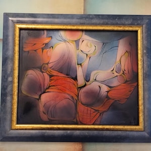 May include: Abstract artwork in a rectangular frame. The painting features a blend of colors, including orange, blue, and purple. The frame has a dark blue outer edge and a gold inner edge. The artwork appears to be an abstract composition.