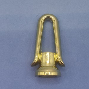 May include: A shiny gold-colored metal eye bolt with a rounded top and a flared base. The eye bolt is designed for attaching to a surface and is likely used for hanging or securing items. The object is set against a blue background.