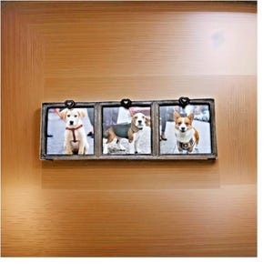May include: A horizontal triple photo frame with a dark metallic finish and three small heart-shaped accents at the top. The frame holds three separate square photographs, each featuring a different dog: a light-colored puppy, a beagle, and a corgi.