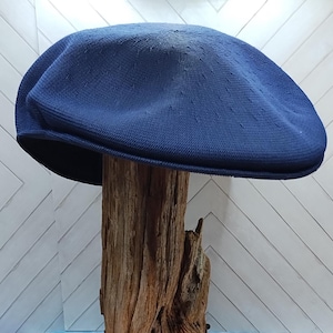 Op de afbeelding: Een effen marineblauwe platte pet met een textuur van geweven stof, een ronde kroon en een korte, verstevigde klep. De pet heeft een consistente diepblauwe kleur en een gestructureerde vorm die een glad en gebogen profiel behoudt.