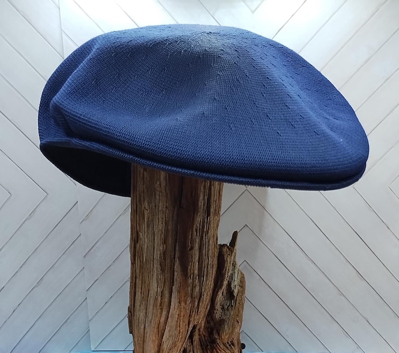 Op de afbeelding: Een effen marineblauwe platte pet met een textuur van geweven stof, een ronde kroon en een korte, verstevigde klep. De pet heeft een consistente diepblauwe kleur en een gestructureerde vorm die een glad en gebogen profiel behoudt.