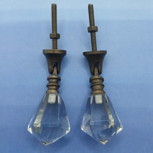 May include: Two clear glass diamond-shaped drawer pulls with a brass finish and screws.