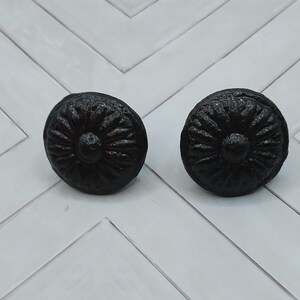 May include: Two black cast iron drawer pulls with a floral design. The pulls are round and have a raised center.