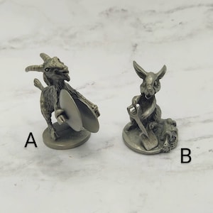 May include: Two pewter figurines, one of a goat playing cymbals and the other of a rabbit holding a shovel. The figurines are on a white background.