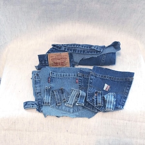 May include: Assorted pieces of denim fabric, including pockets, belt loops, and sections of jeans. A Levi Strauss & Co. label is visible. The denim is a medium blue wash, with some pieces rolled or folded.