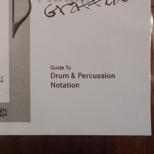 Könnte beinhalten: Ein schwarz-weißes Handbuch zur Notation von Schlagzeug und Percussion. Das Cover zeigt eine stilisierte Musiknote und den Text "Audiograffiti" in einer handschriftlichen Schrift.