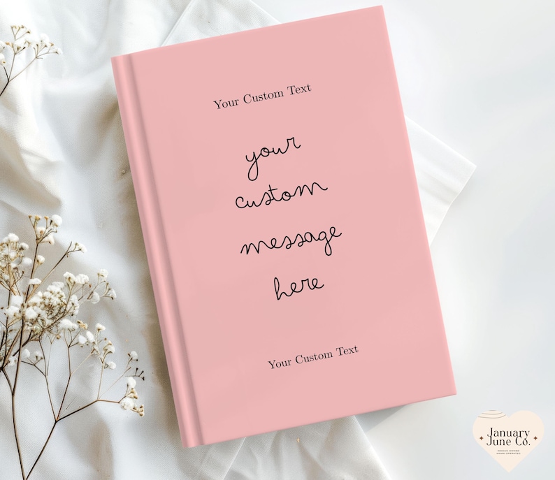 Puede incluir: Un diario de tapa dura rosa claro con el texto "Your Custom Text" en la parte superior e inferior, y "your custom message here" en el centro. El diario est&aacute; sobre una tela blanca con peque&ntilde;as flores blancas.