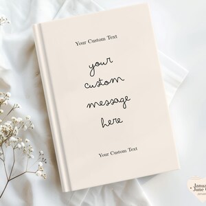 Puede incluir: Un libro color crema con el texto "Your Custom Text" en la parte superior e inferior. Las palabras "your custom message here" est&aacute;n escritas en cursiva en el centro del libro. El libro est&aacute; sobre una superficie blanca.