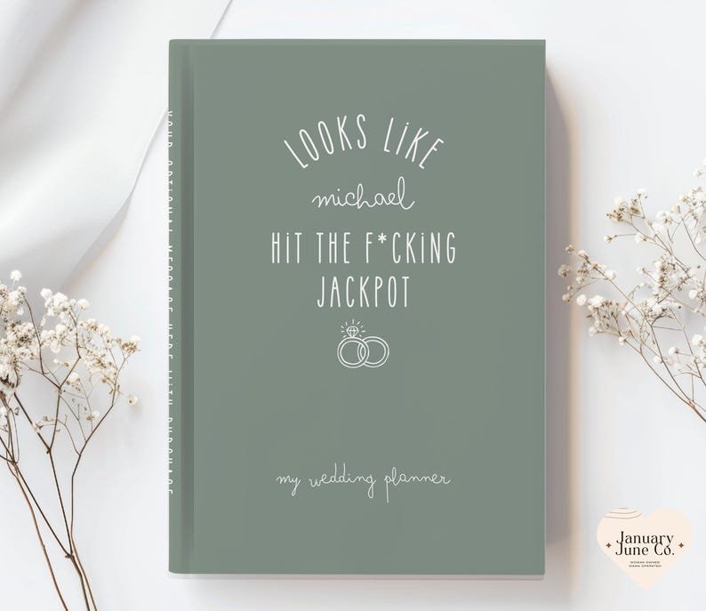 K&ouml;nnte beinhalten: Ein hellgr&uuml;ner Hochzeitsplaner mit wei&szlig;em Text, der "LOOKS LIKE michael HIT THE F*CKING JACKPOT" und "my wedding planner" lautet. Das Cover zeigt auch zwei Eheringe. Der Planer ist ein Hardcover-Buch.