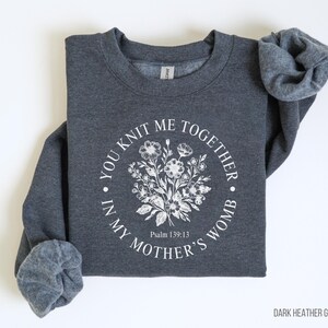 May include: Dark heather grey sweatshirt with a white floral design and the text "You knit me together in my mother's womb" and "Psalm 139:13".