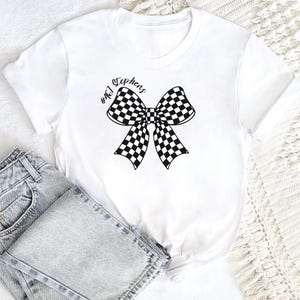 May include: White t-shirt with a black and white checkered bow and the text "#461 Stephens" printed on the front.