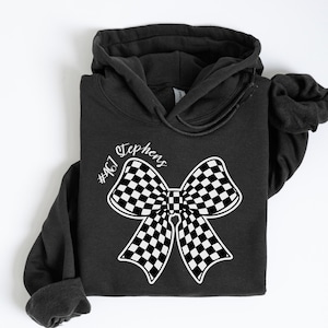 May include: Black hooded sweatshirt with a white checkered bow and the text "Stephens #407" printed on the front.
